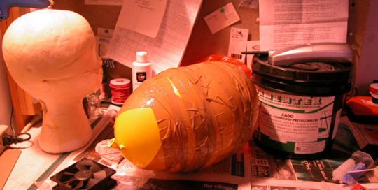 Orange latex lung and mannequin head on a cluttered desk in red light