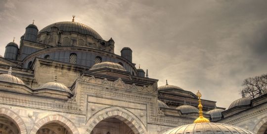 Mosque dome and arched courtyard under a dramatic cloudy sky