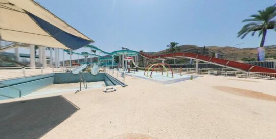 Still from a 360 tour of the closed Gai Beach Water Park in Tiberias, July 2020: an empty pool, water slides and a palm tree under a blue sky
