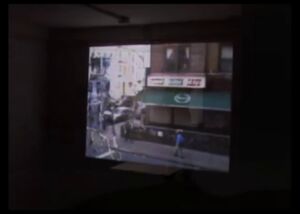 Still from the video [rift]: a darkened room with a street scene projected on the far wall