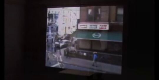 Still from the video [rift]: a darkened room with a street scene projected on the far wall